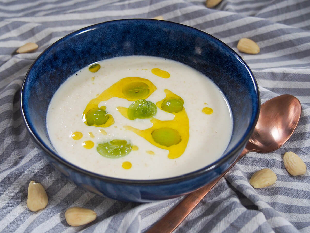 bowl of ajo blanco with spoon to side and grapes garnishing soup