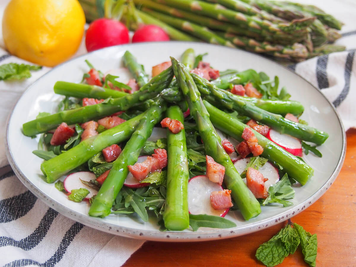 side view of asparagus salad with lemon vinaigrette with asparagus spears stacked into middle of plate