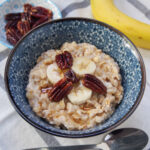 bowl of banana oatmeal topped with slices of banana and pecans