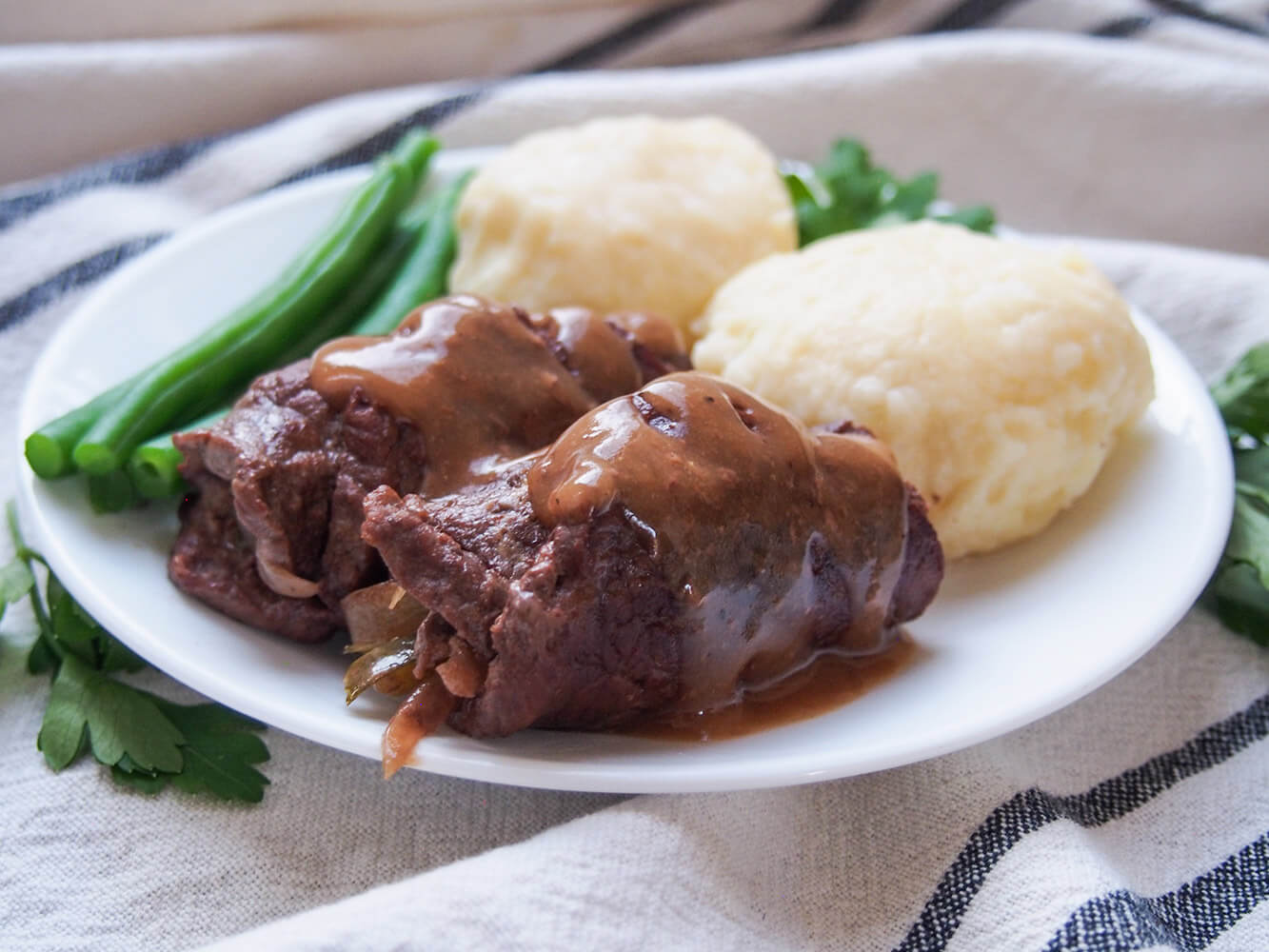 side view of beef rouladen topped with gravy with sides behind