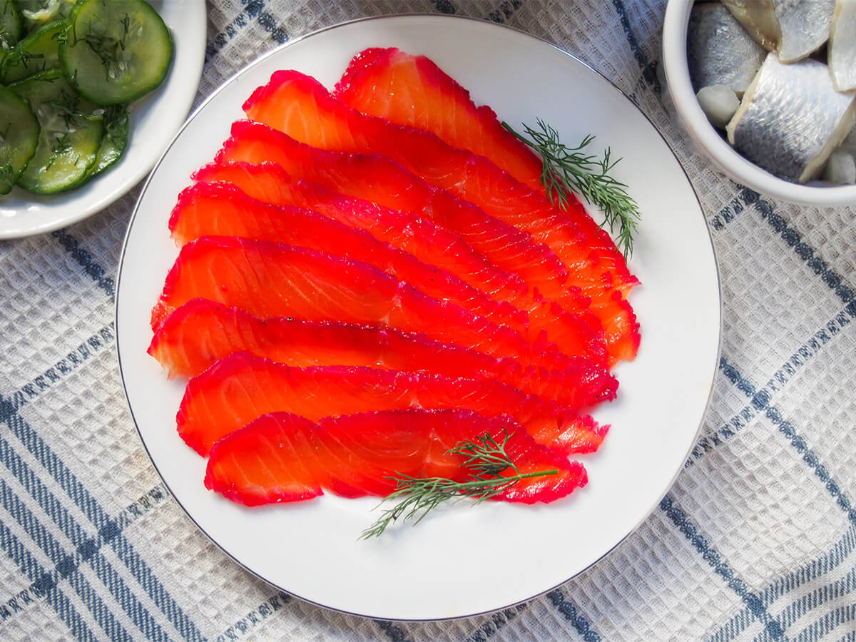 plate of beet cured salmon gravlax with corners of bowls with herring and cucumber