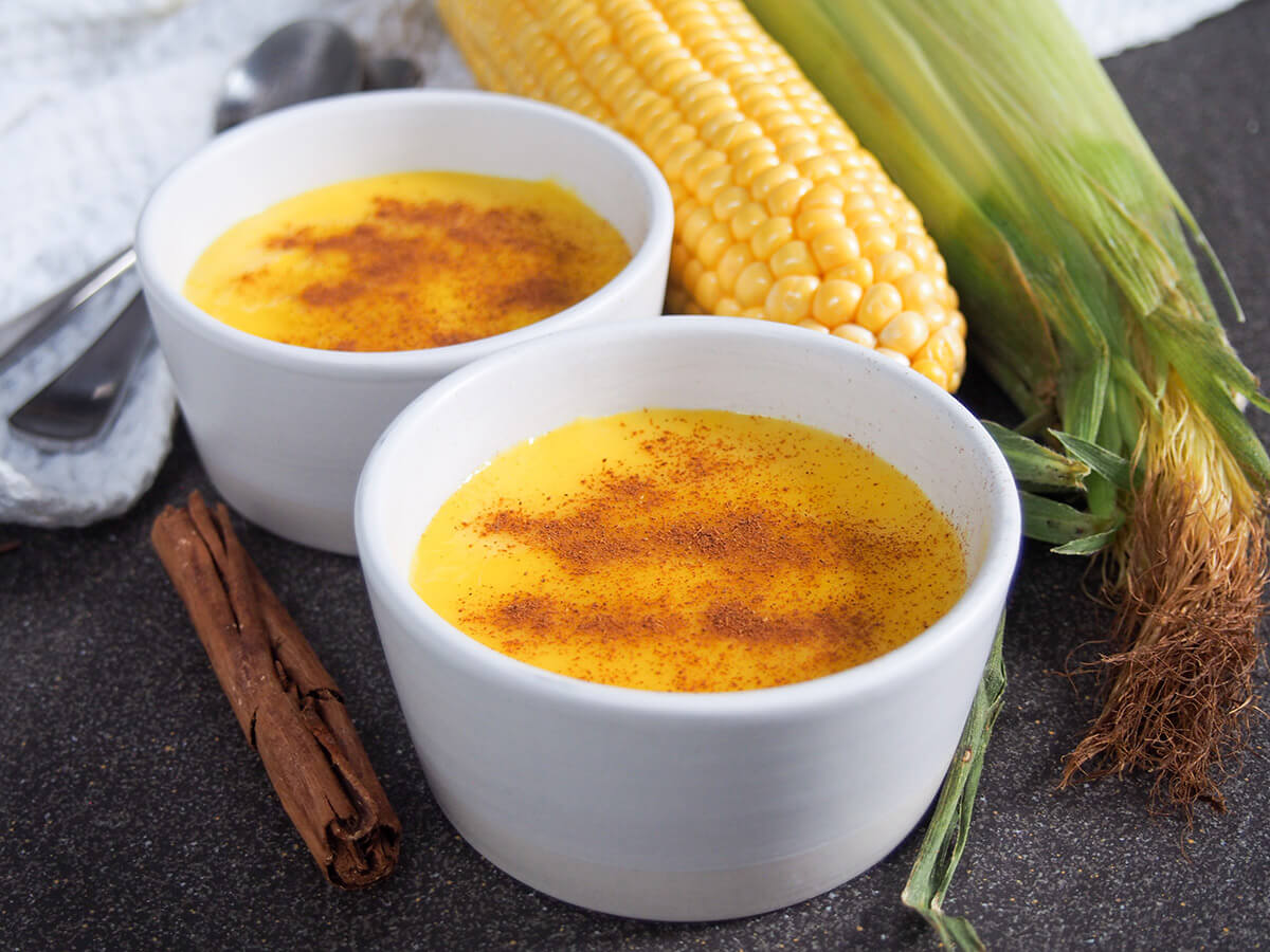 two dishes of Brazilian corn pudding with corn behind and cinnamon stick to side