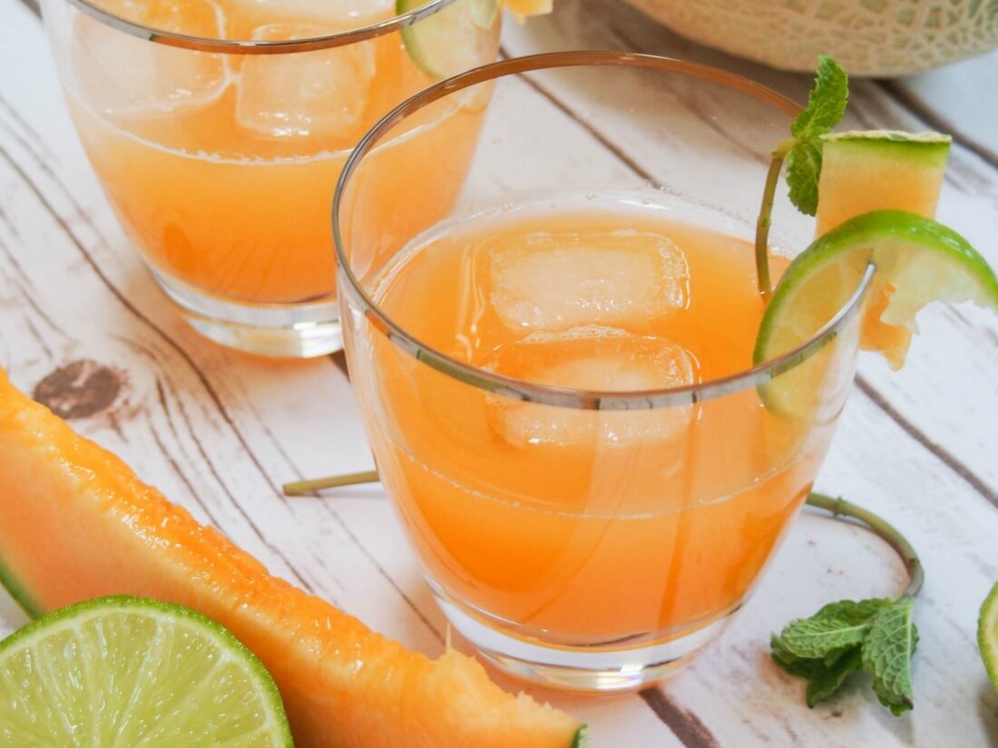 glass of cantaloupe agua fresca with slice of cantaloupe ad lime in front