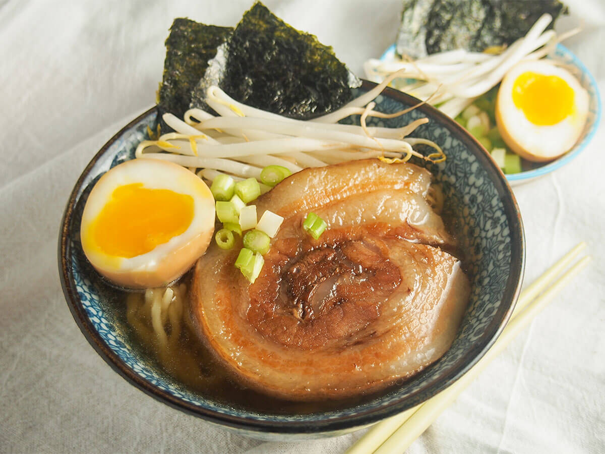 chashu pork on top of ramen bowl with additional toppings behind