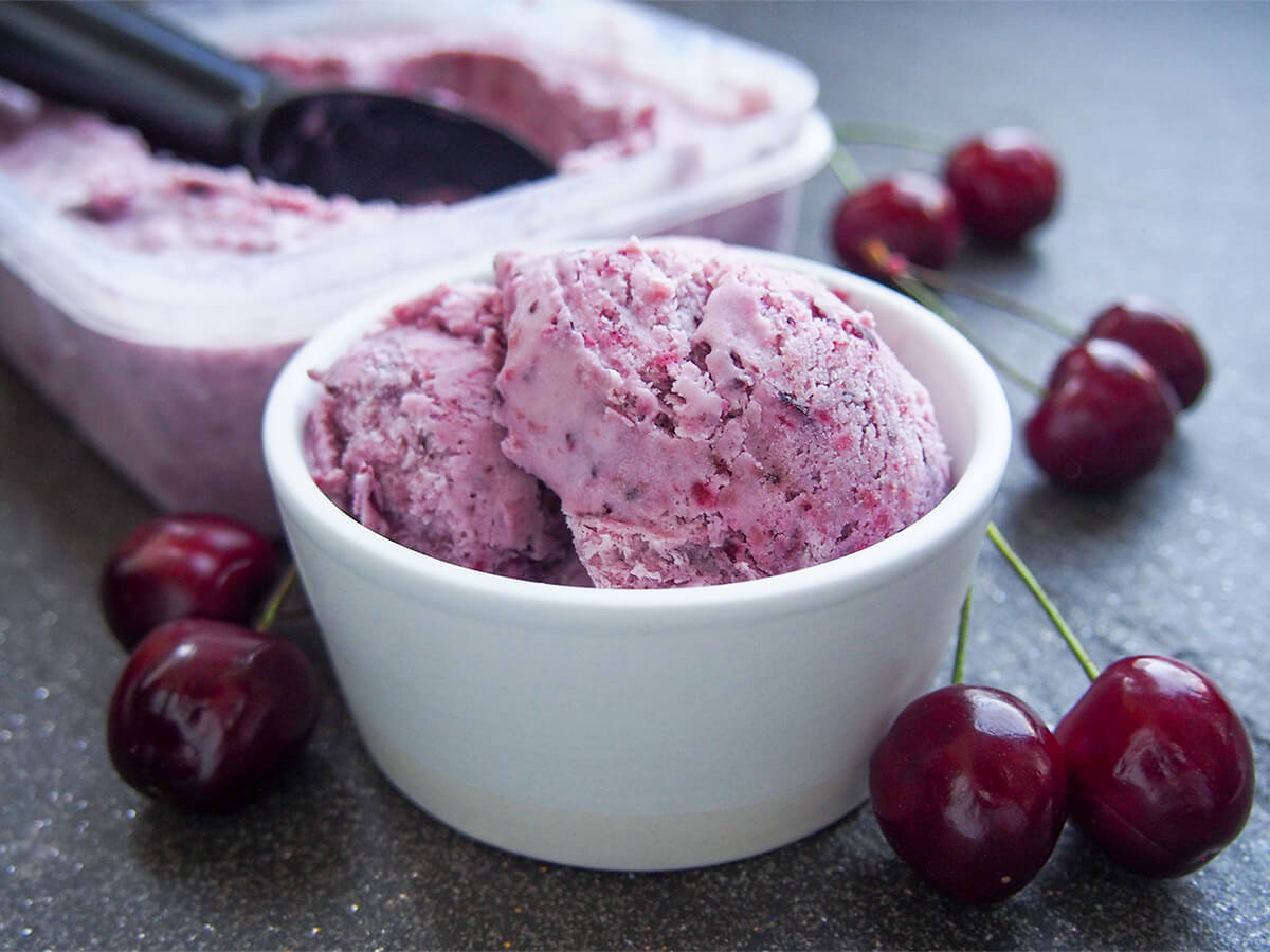 bowl of cherry ice cream with cherries around bowl and tub behind