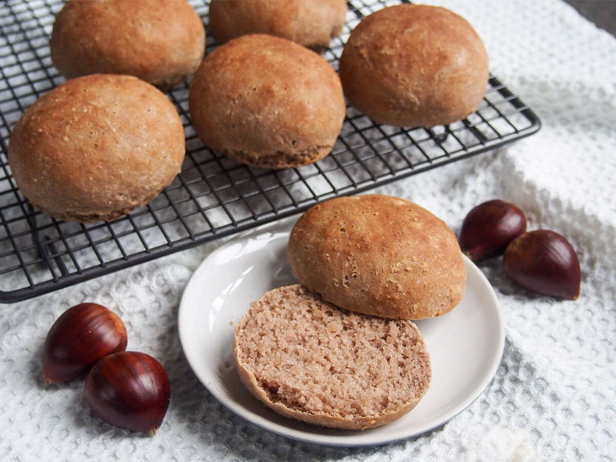 sliced open chestnut bread roll on plate with chestnuts to side and rolls on rack behind