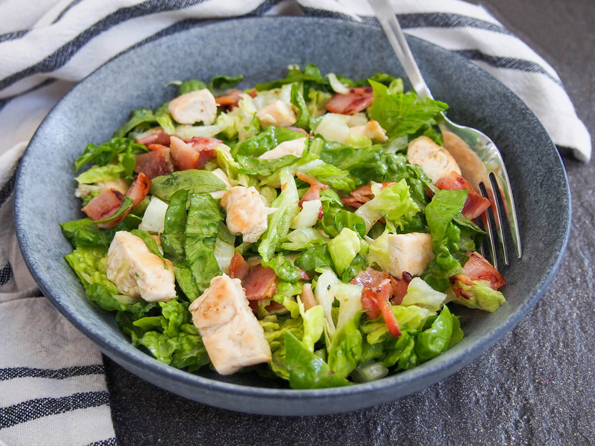 bowl of chicken and bacon salad viewed from front with fork inside bowl to one side