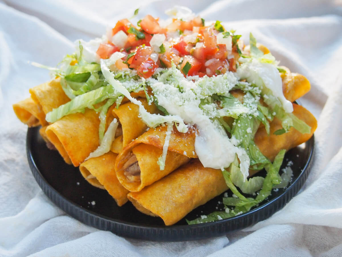 plate of chicken flautas loaded with lettuce, pico de gallo, cream and cheese on top