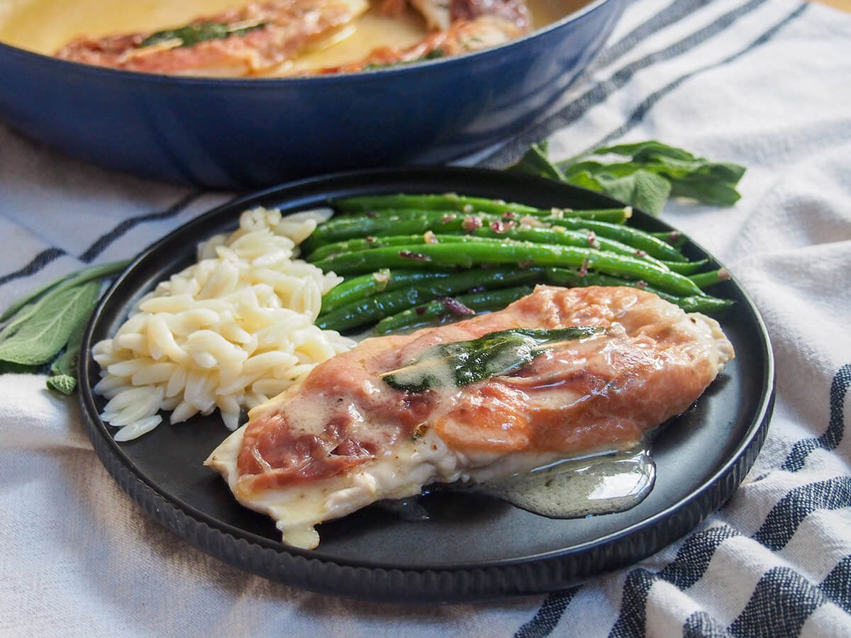 plate of chicken saltimbocca with green beans and orzo behind