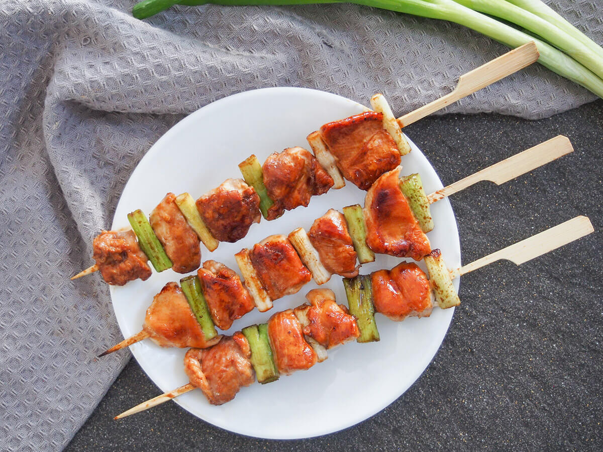 plate of chicken yakitori from above with spring onions above plate