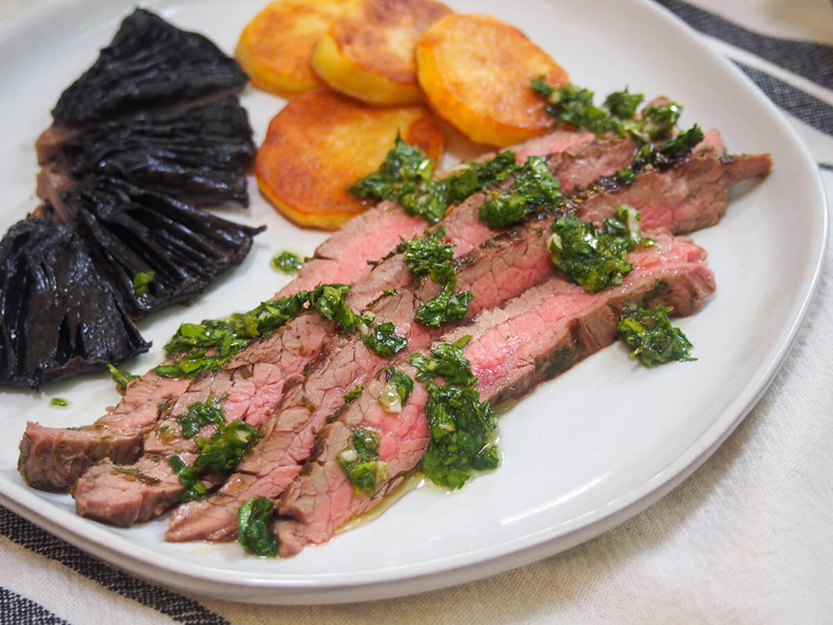 chimichurri marinated steak on plate with potatoes and portobello mushroom behind