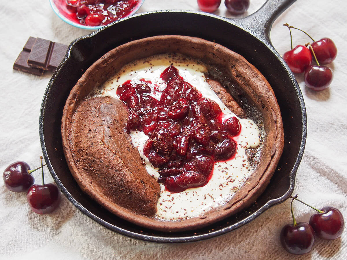 skillet with chocolate Dutch baby pancake topped with cherry compote