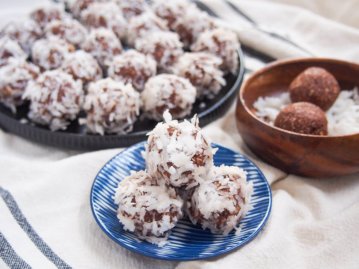 small stack of chokladbollar with plate of the chocolate oat balls behind