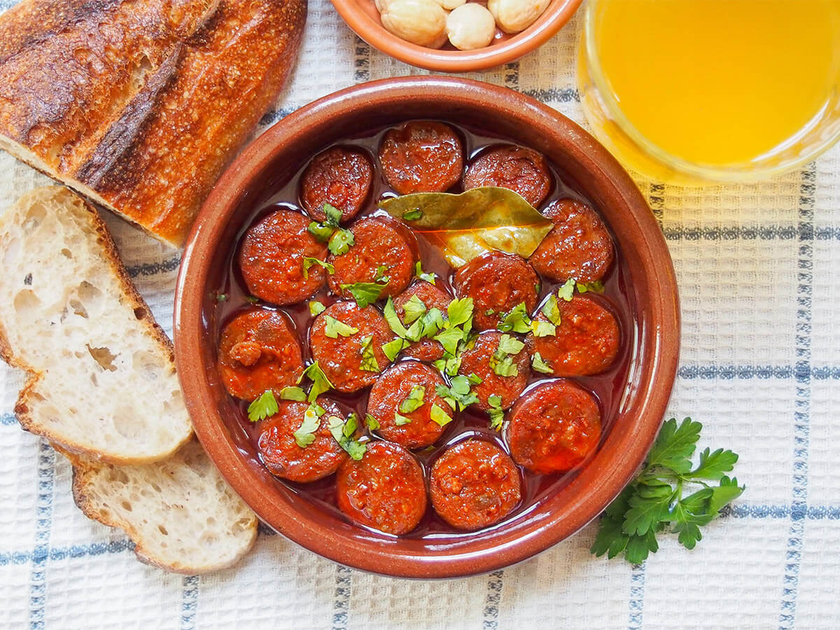 dish of chorizo a la sidra (chorizo in cider) with bread to one side and cider to other