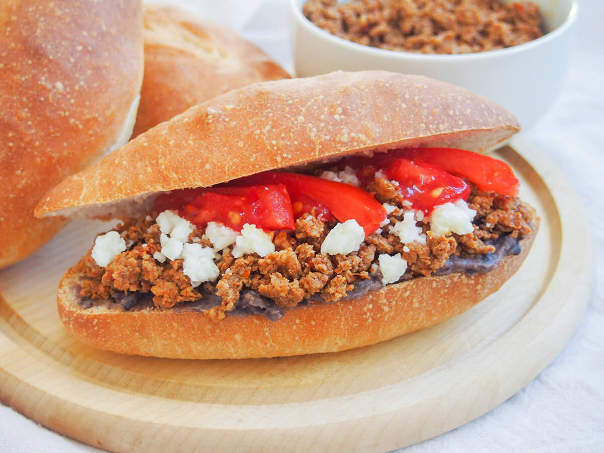 chorizo torta on wooden board with rolls and chorizo behind