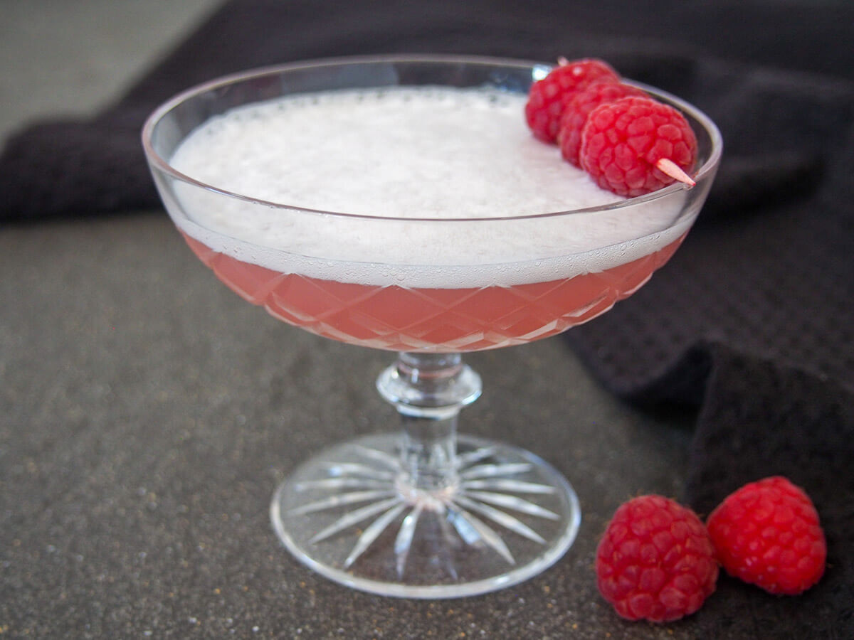 glass of Clover club in Paris - a gin cocktail - topped with raspberries on a cocktail stick