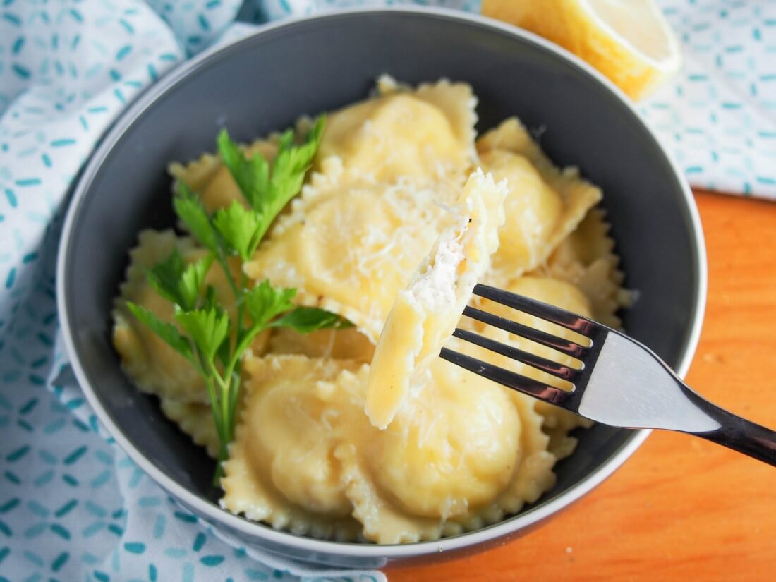 crab ravioli with one bitten into held on fork over bowl