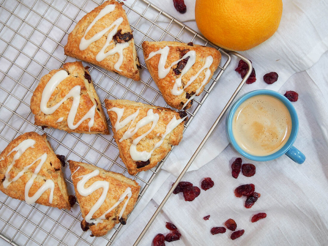 Cranberry orange scones with cup of coffee and orange to side from overhead