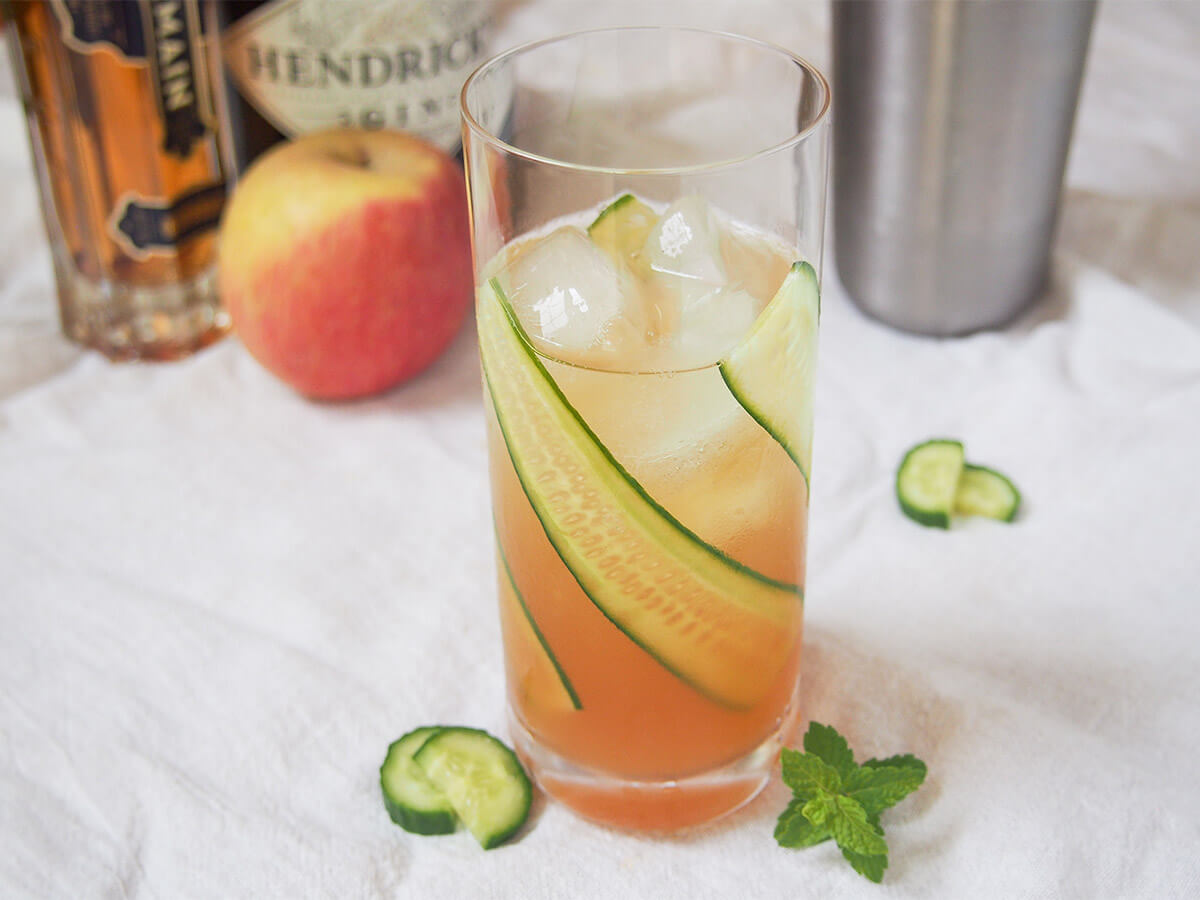 glass of English garden cocktail with apple, cocktail shaker and bottles behind