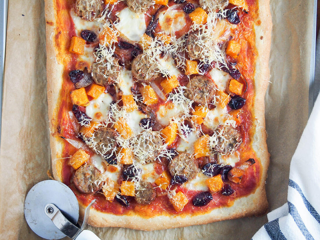 fall pizza with sausage and squash with pizza cutter to side