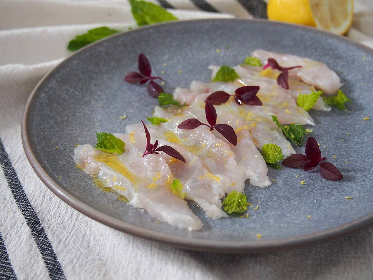 plate of fish crudo decorated with microgreens and mint from side