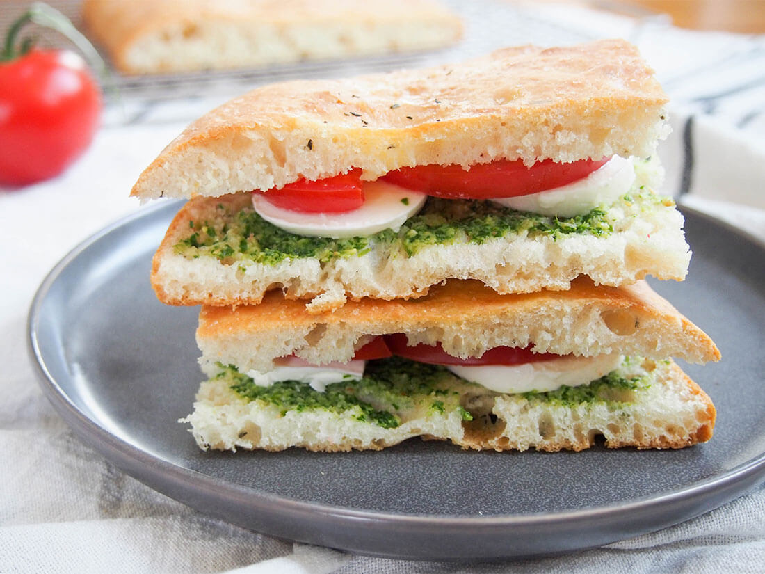caprese focaccia sandwich on plate with additional bread in background