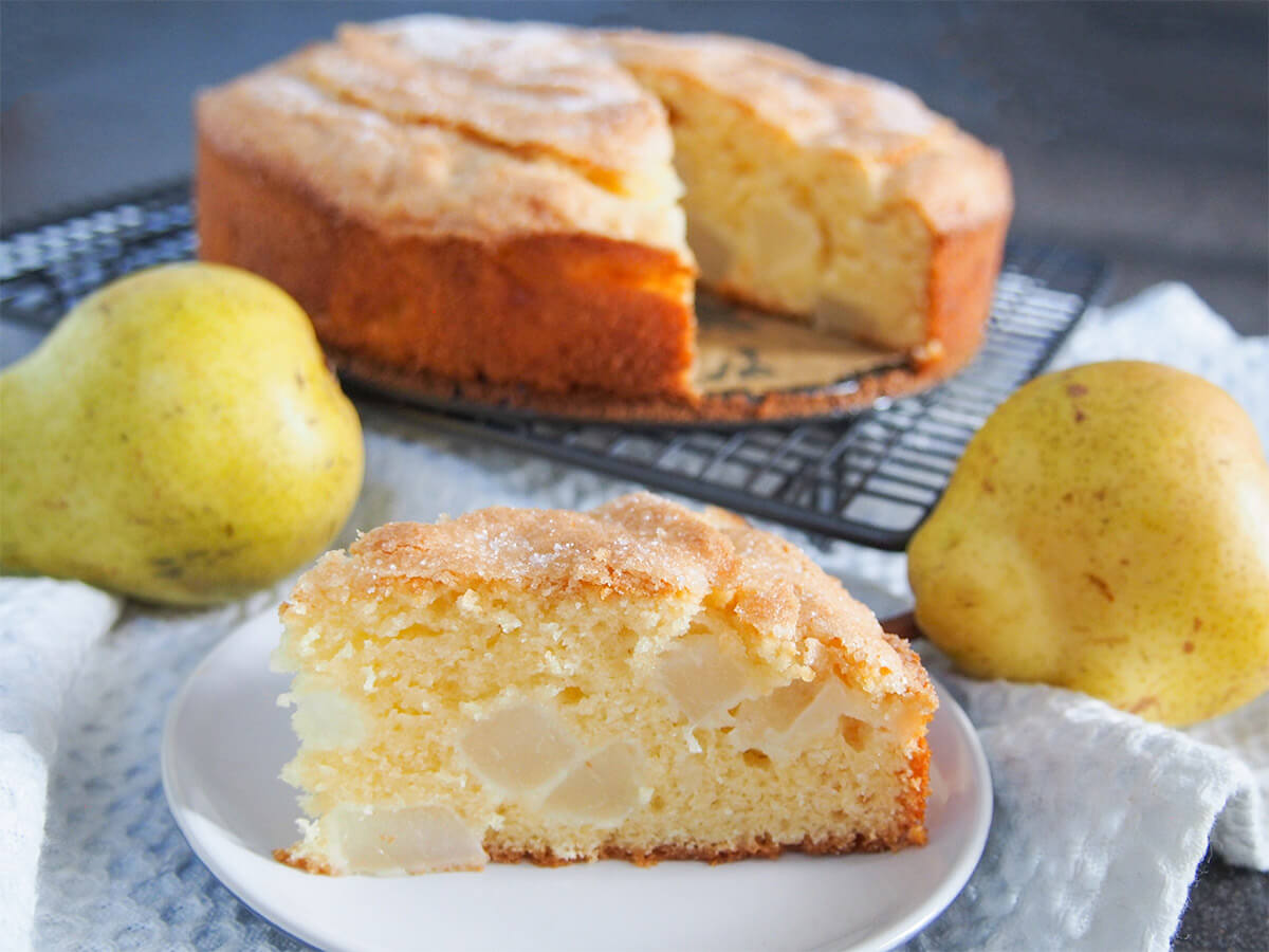 slice of French pear cake in front of rest of cake with pears to sides