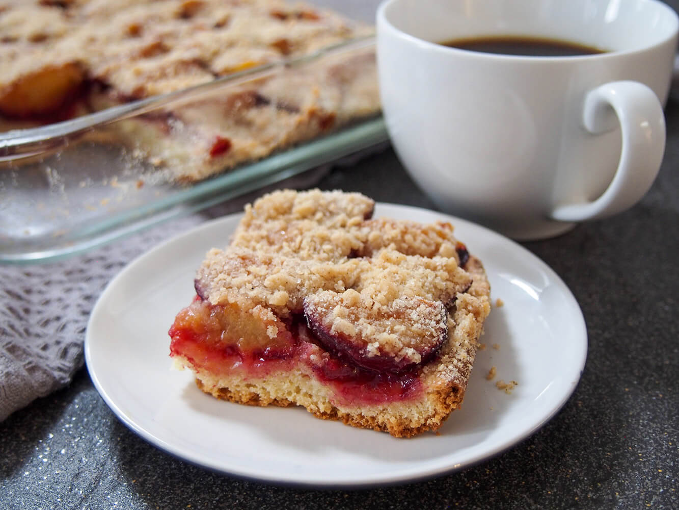 slice of German plum cake (pflaumenkuchen) with cup of coffee to side