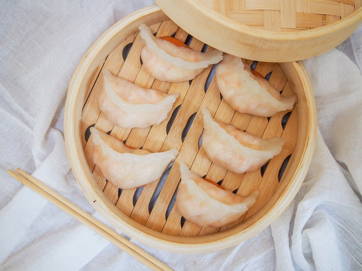 har gow crystal shrimp dumplings in steamer basket form overhead with chopsticks below.