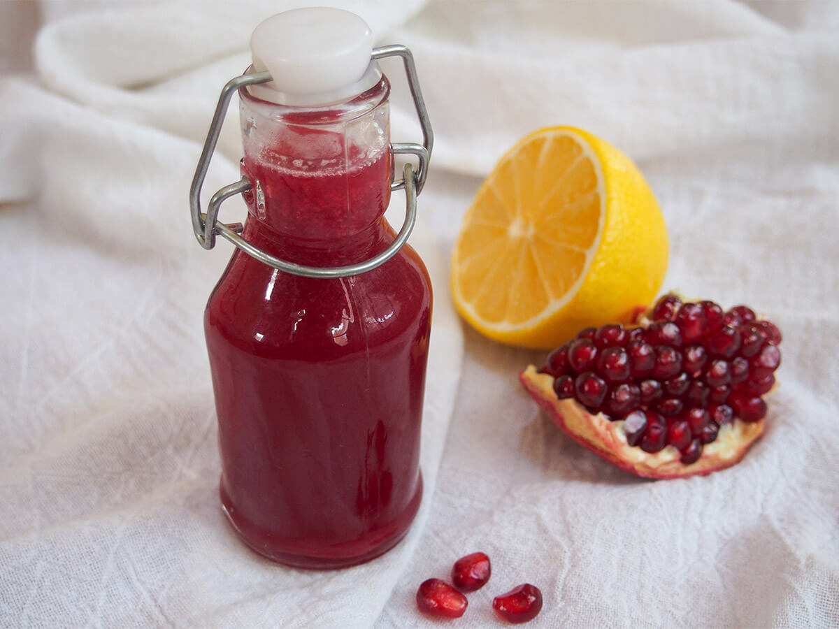 small bottle of homemade grenadine with half lemon and piece of pomegranate to side