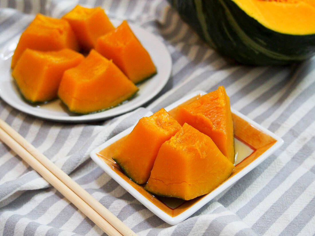 small and larger plates of kabocha no nimono with chopsticks to side