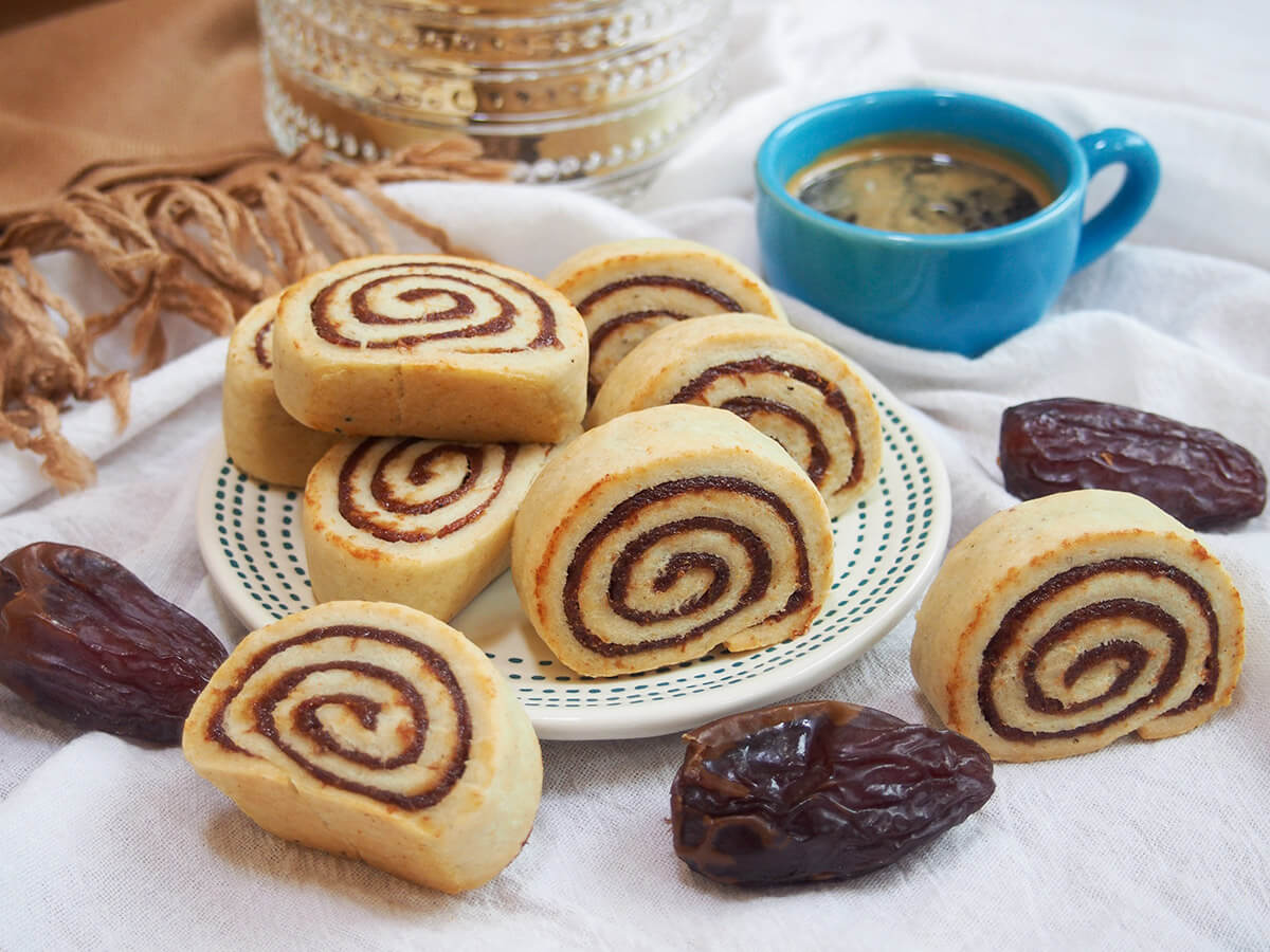 plate of kleicha Iraqi date cookies with coffee cup behind and dates around plate