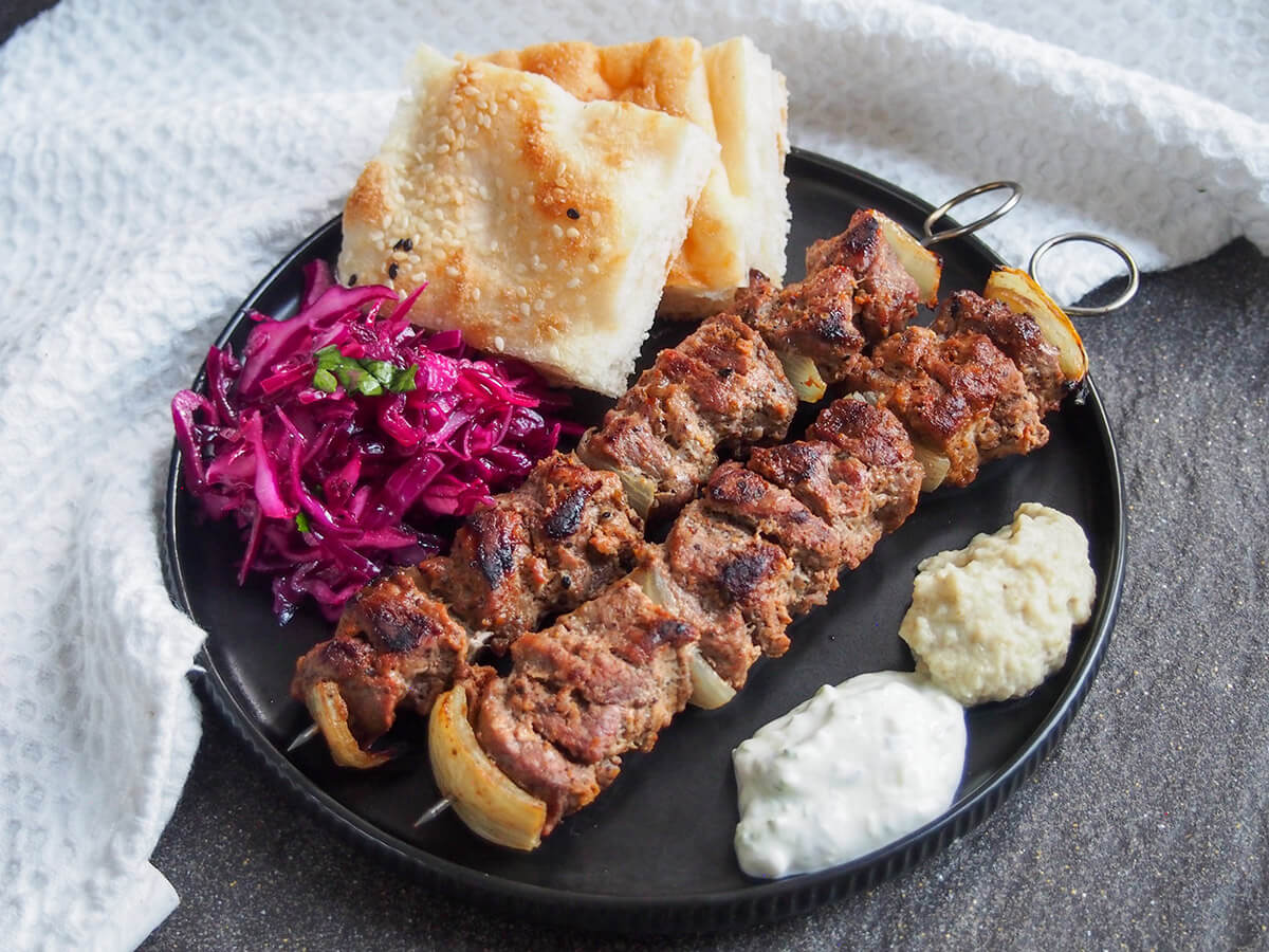 plate with lamb shish kebab, red cabbage, bread and sauces to side