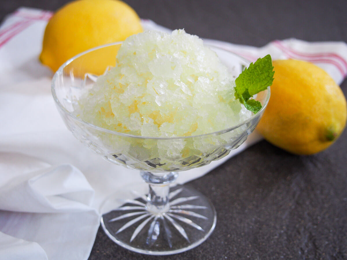 glass of lemon granita with two lemons behind glass