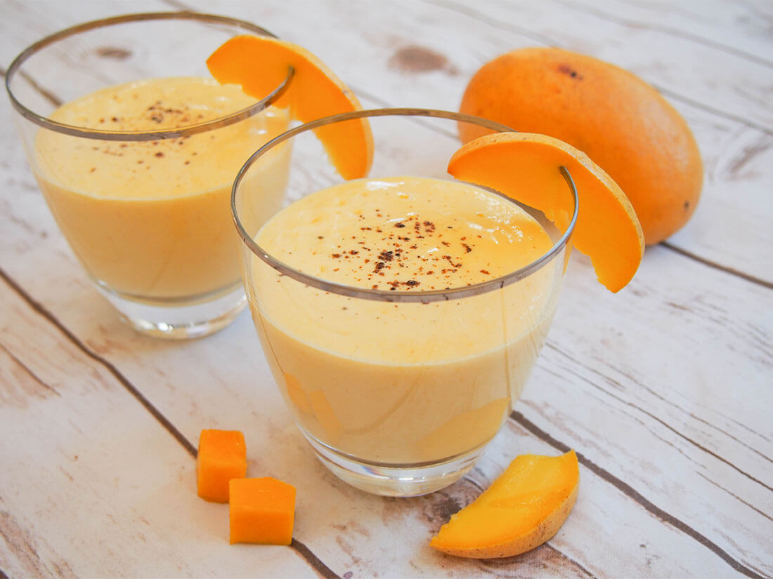 two glasses of mango lassi with pieces of mango to side