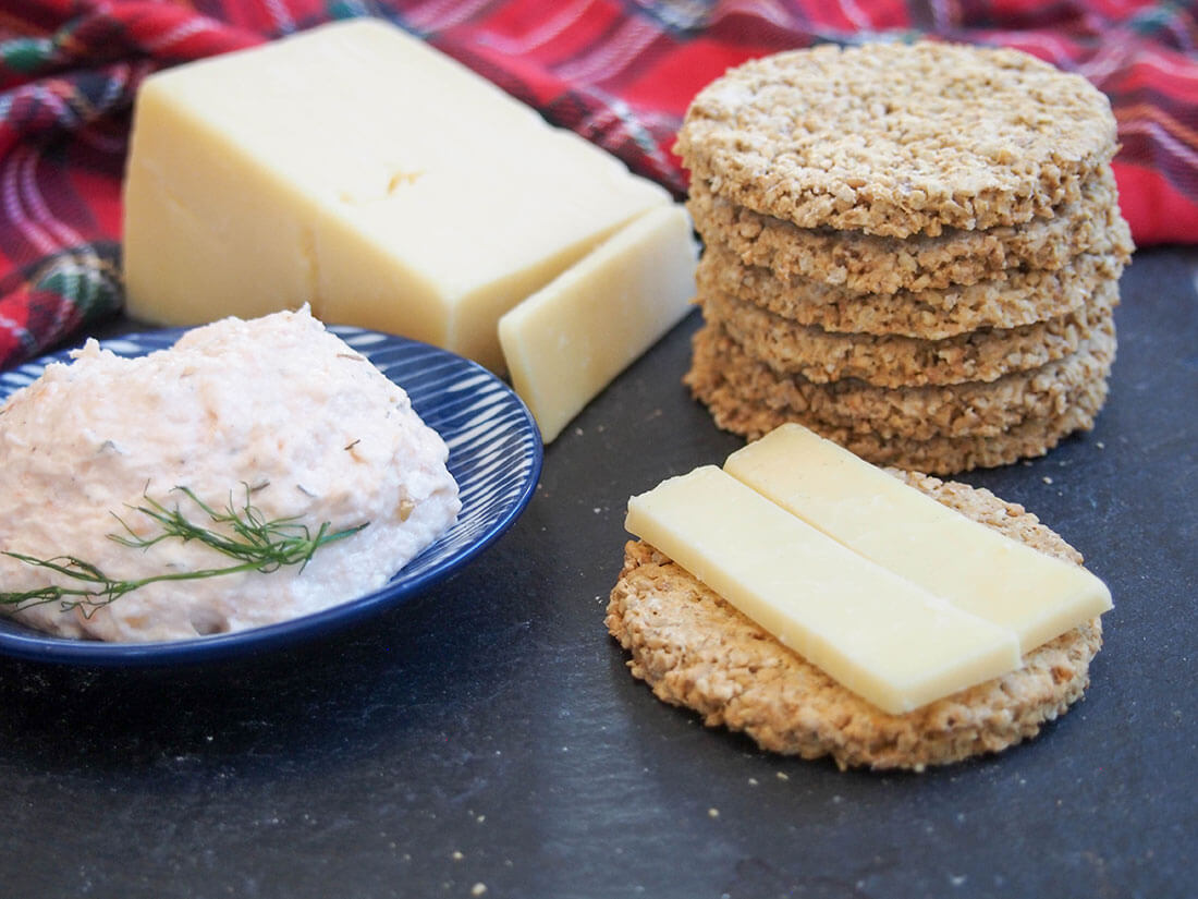 stack of oatcakes to one side with block of cheese and dish with pate to other side