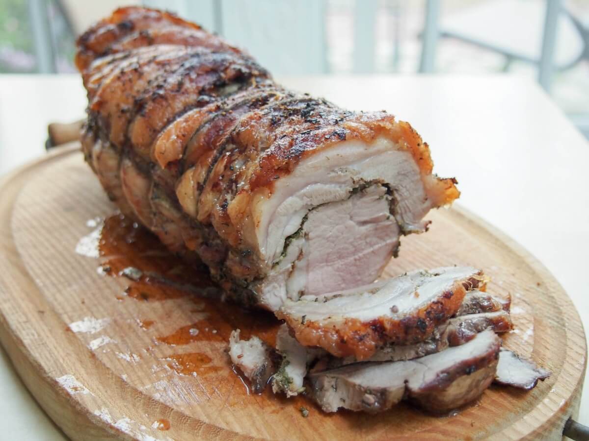 whole porchetta on cutting board with a few slices cut from front