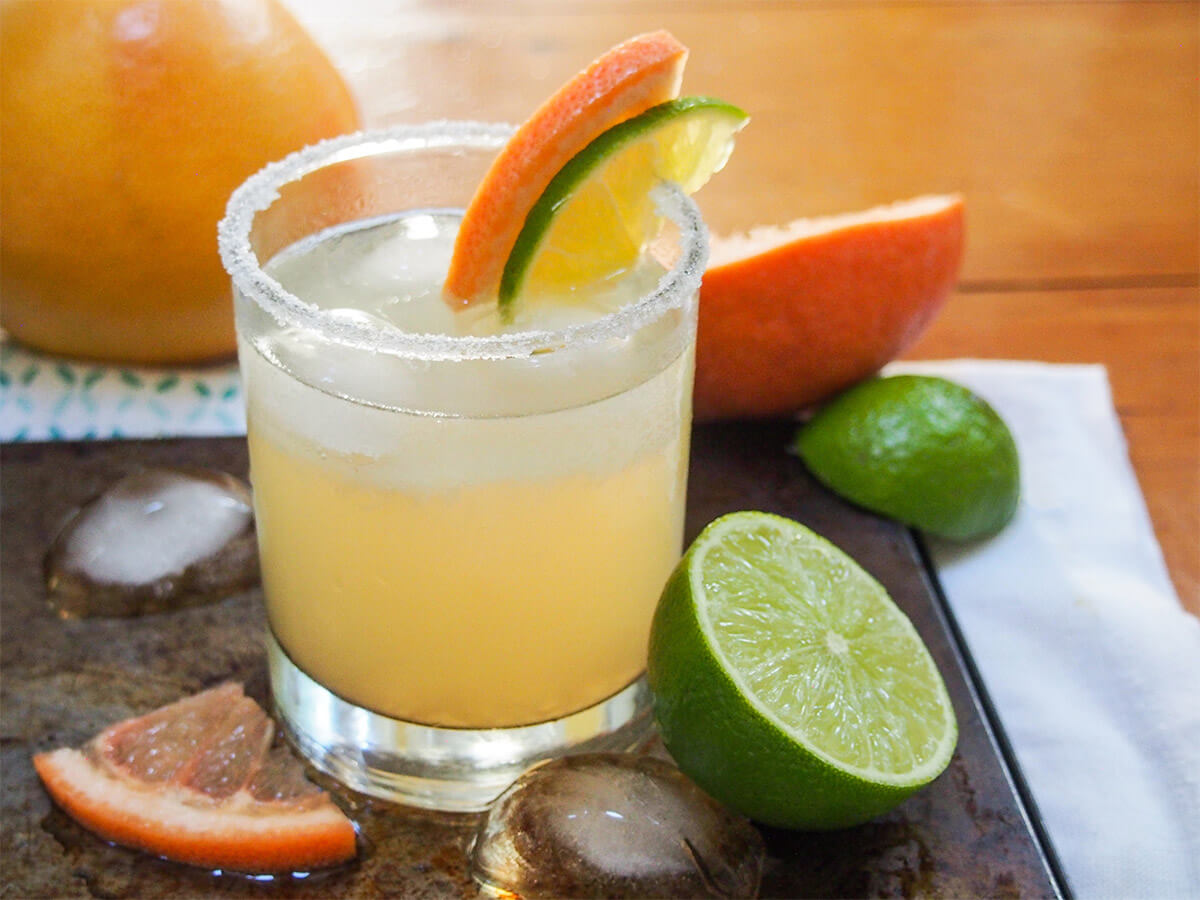 glass of paloma cocktail with half lime and grapefruit to side