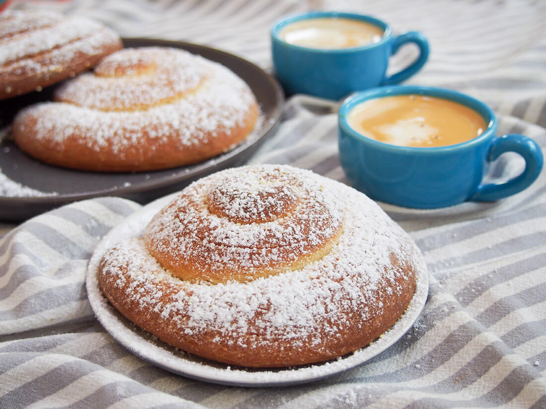 Pan de Mallorca (Puerto Rican sweet rolls) - one on plate with more behind