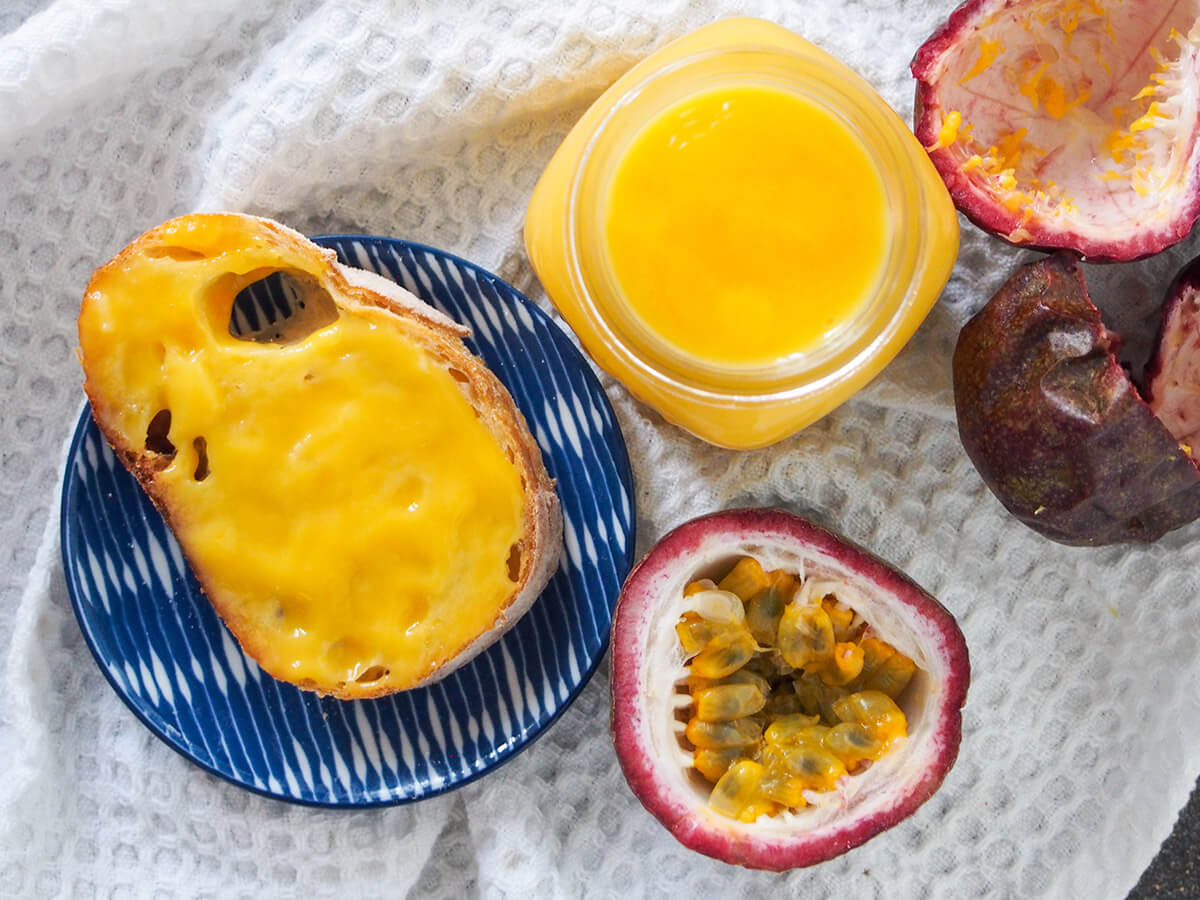 jar of passion fruit curd with bread with curd to side and passion fruit below, empty passion fruit shell to other side