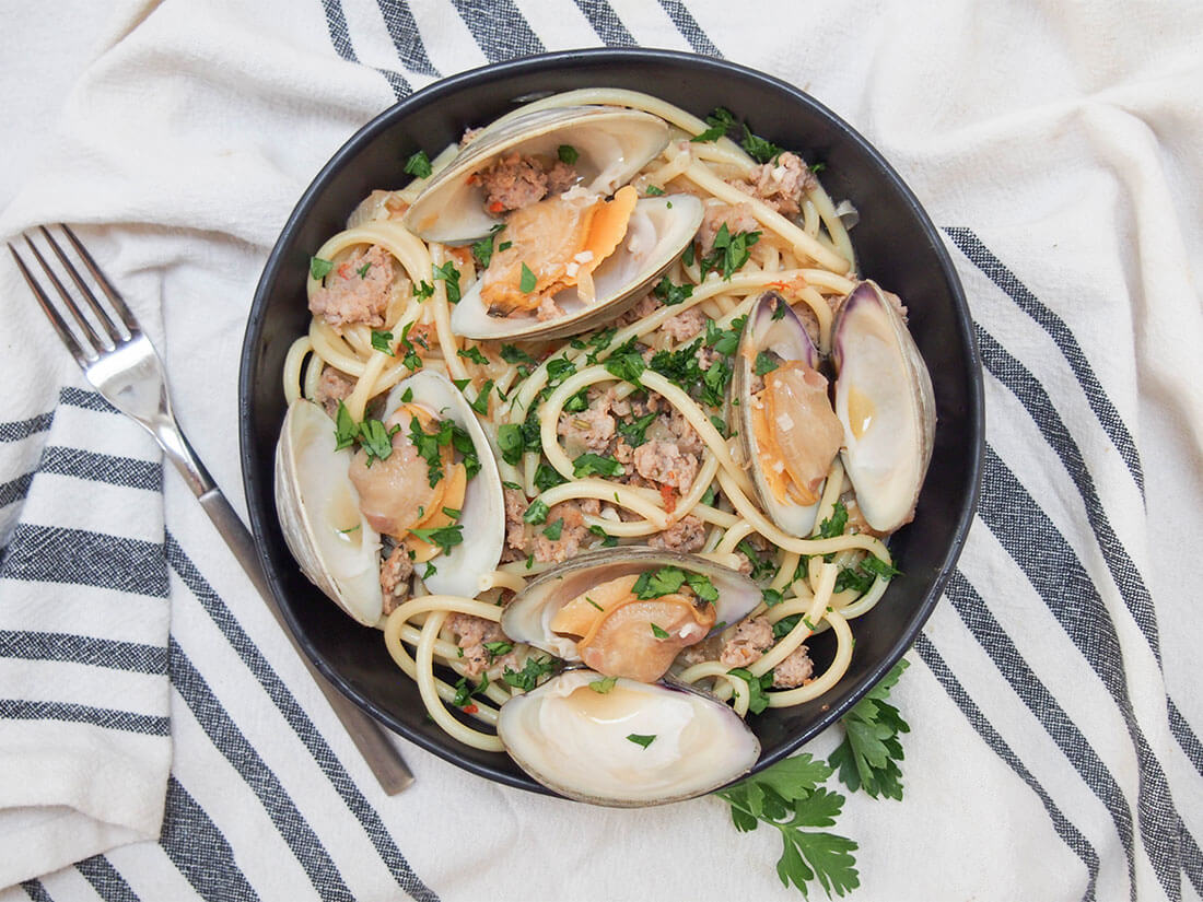 Pasta with clams and sausage in bowl with fork to side viewed from overhead