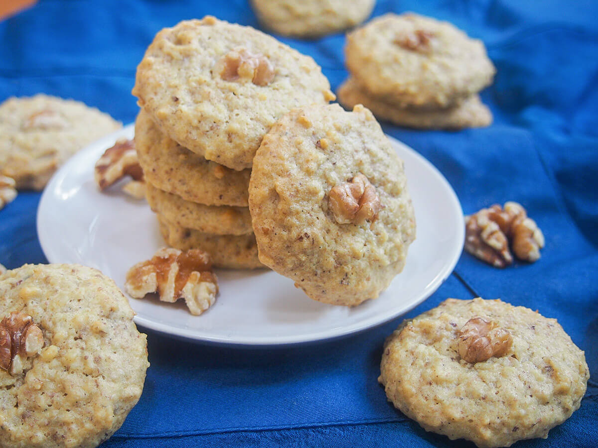 stack of Persian walnut cookies with one to side and more cookies around plate