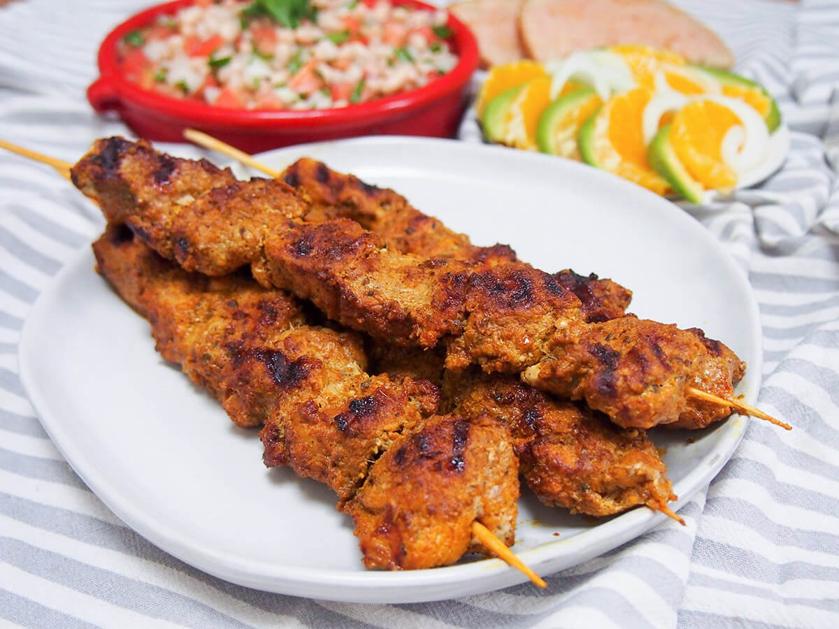 plate of pinchos morunos Spanish pork skewers with salads behind