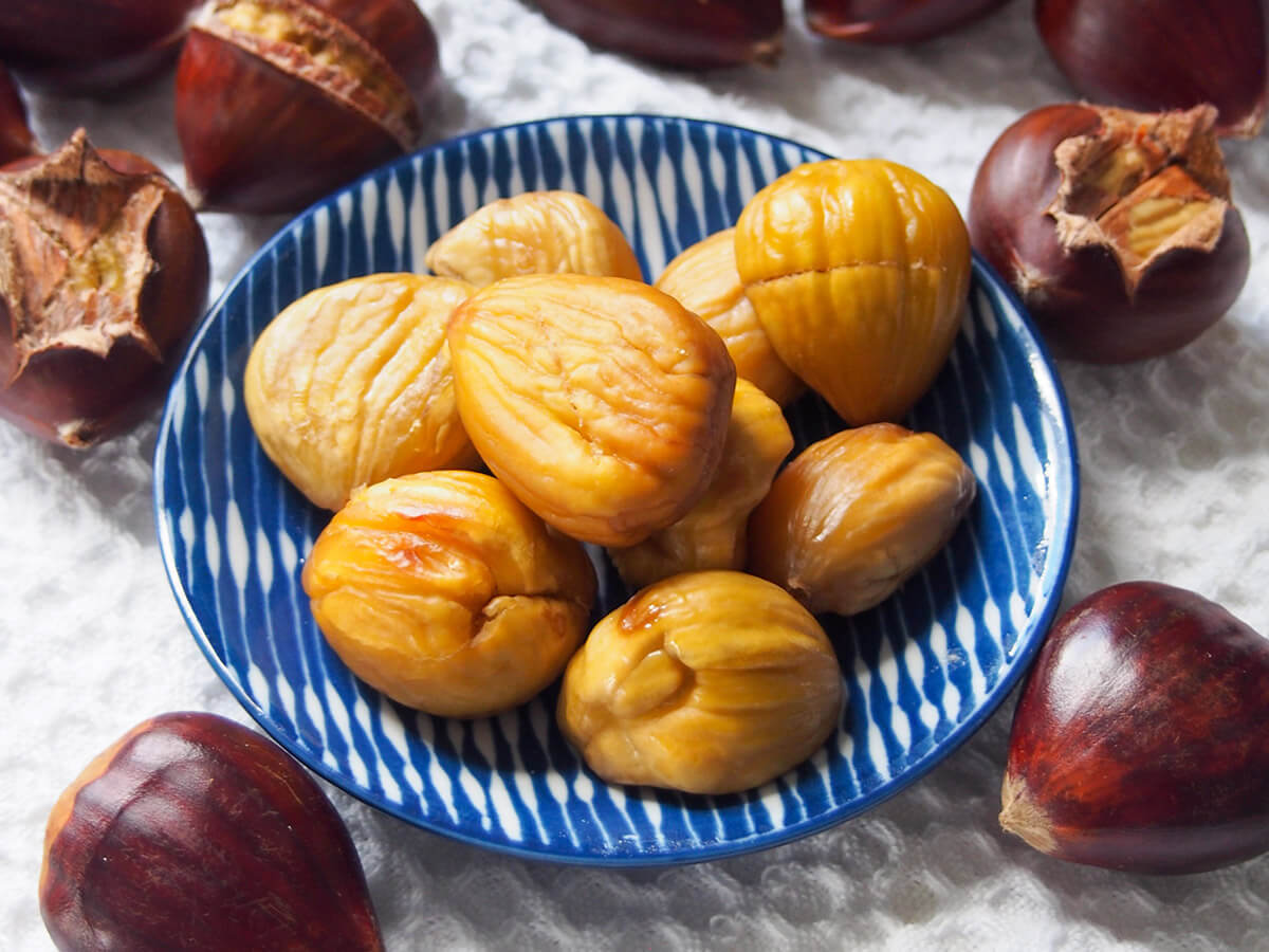 plate of roasted chestnuts with some whole ones and some to peel to side