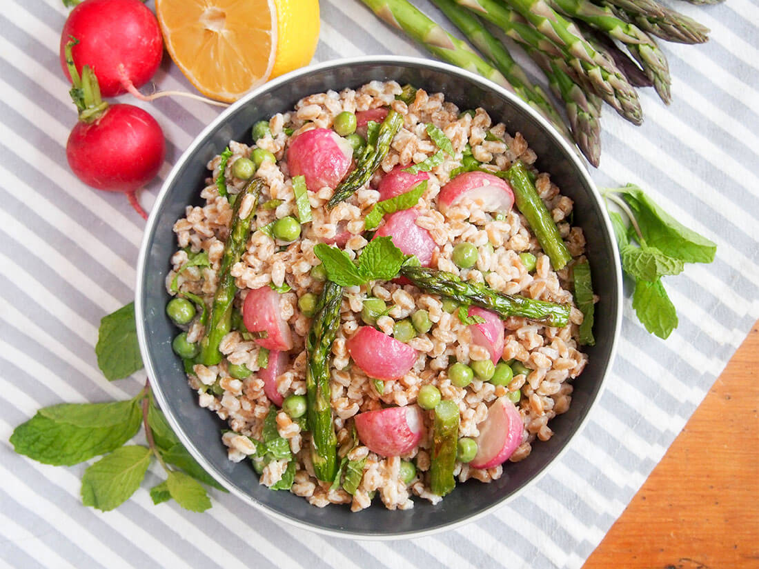 Roasted spring vegetable farro salad in bowl viewed from overhead with ingredients around bowl