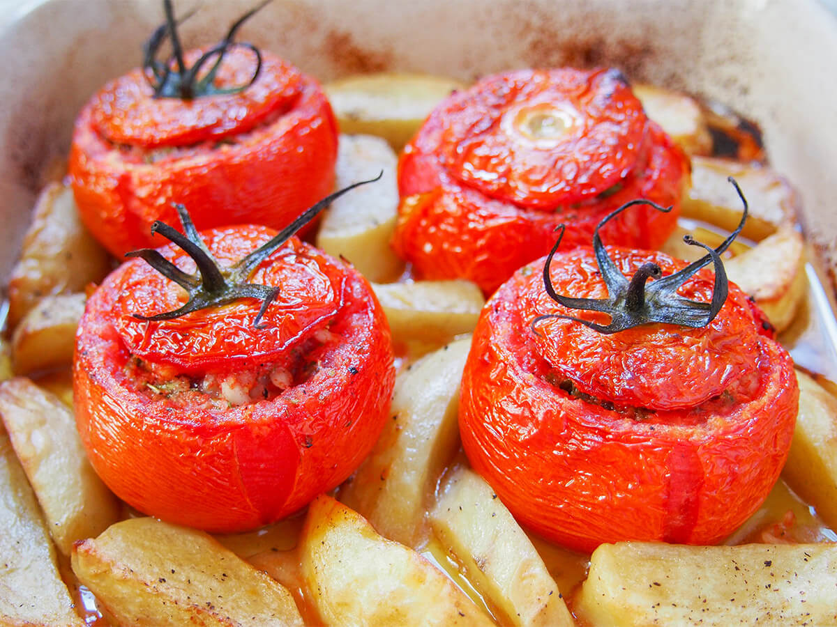 four tomatoes stuffed with rice in dish with potatoes around