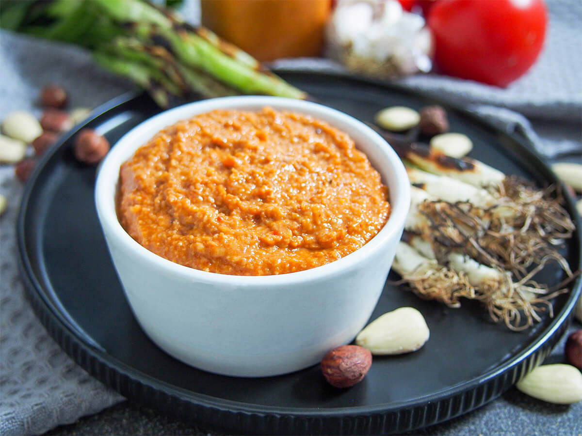 romesco sauce in dish with grilled spring onions on plate behind