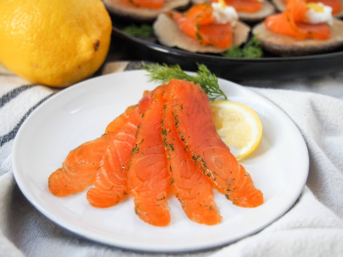 salmon gravlax on plate with a lemon and some gravlax topped blini behind