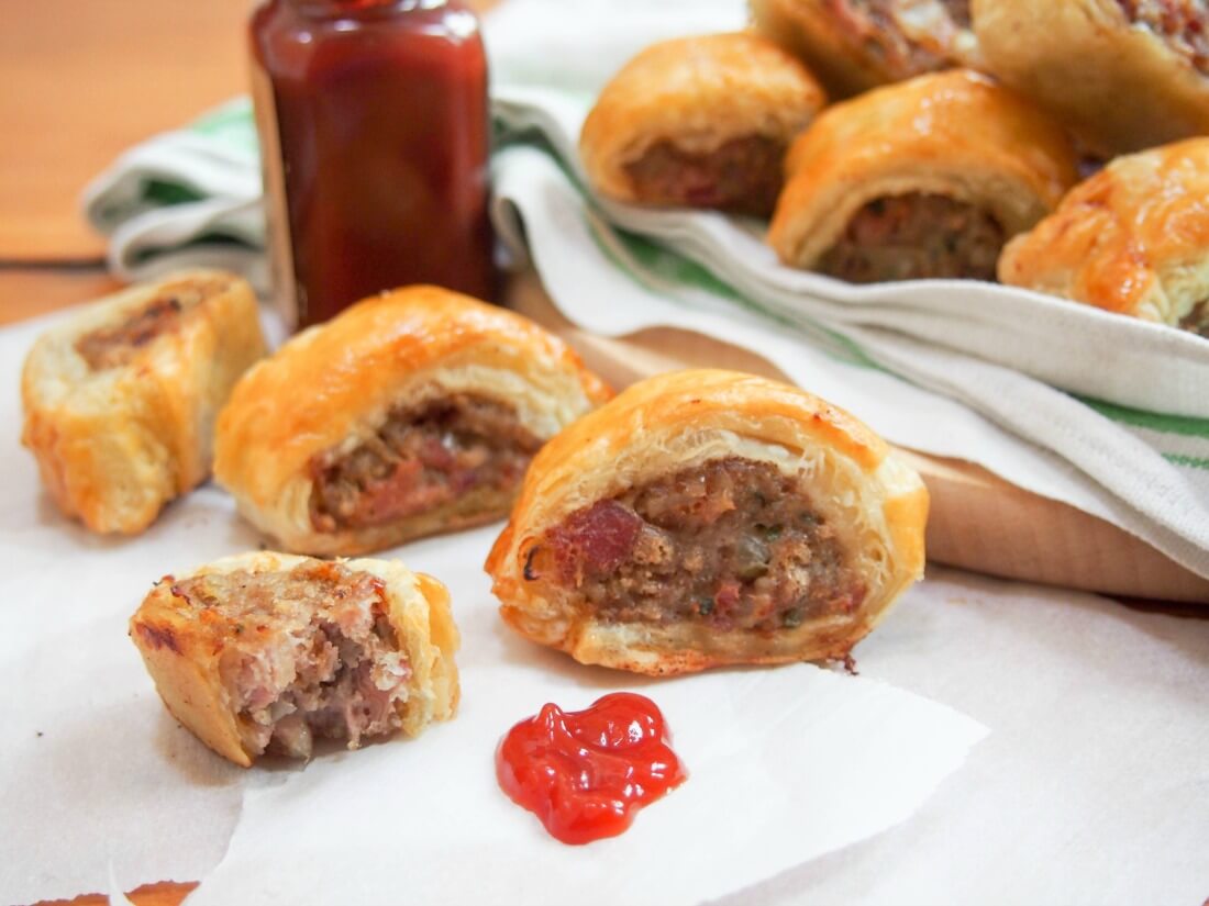 sausage rolls on parchment with stack to side and some tomato ketchup to front