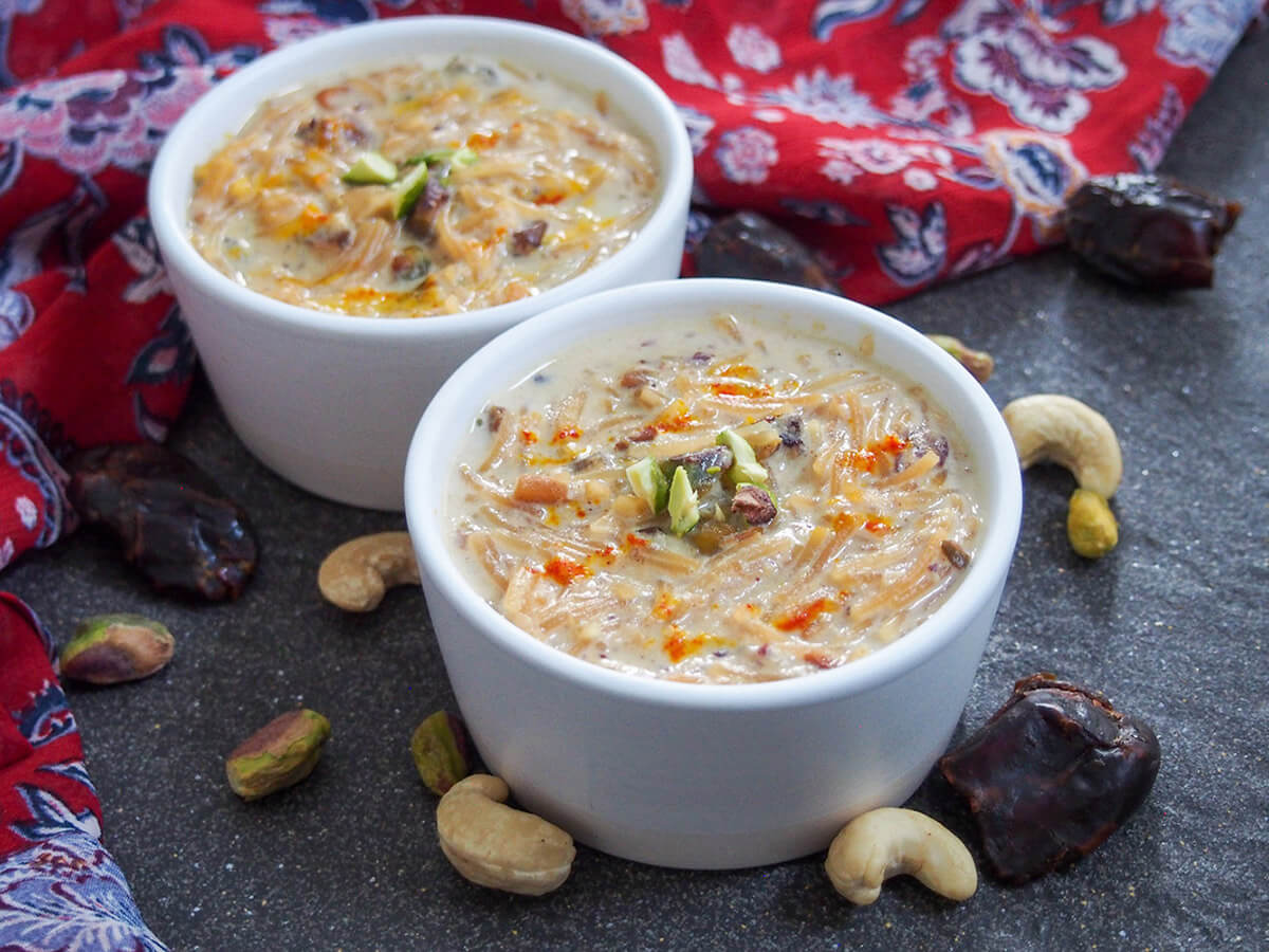 bowl of sheer khurma with a second bowl behind and nuts and dates around bowls